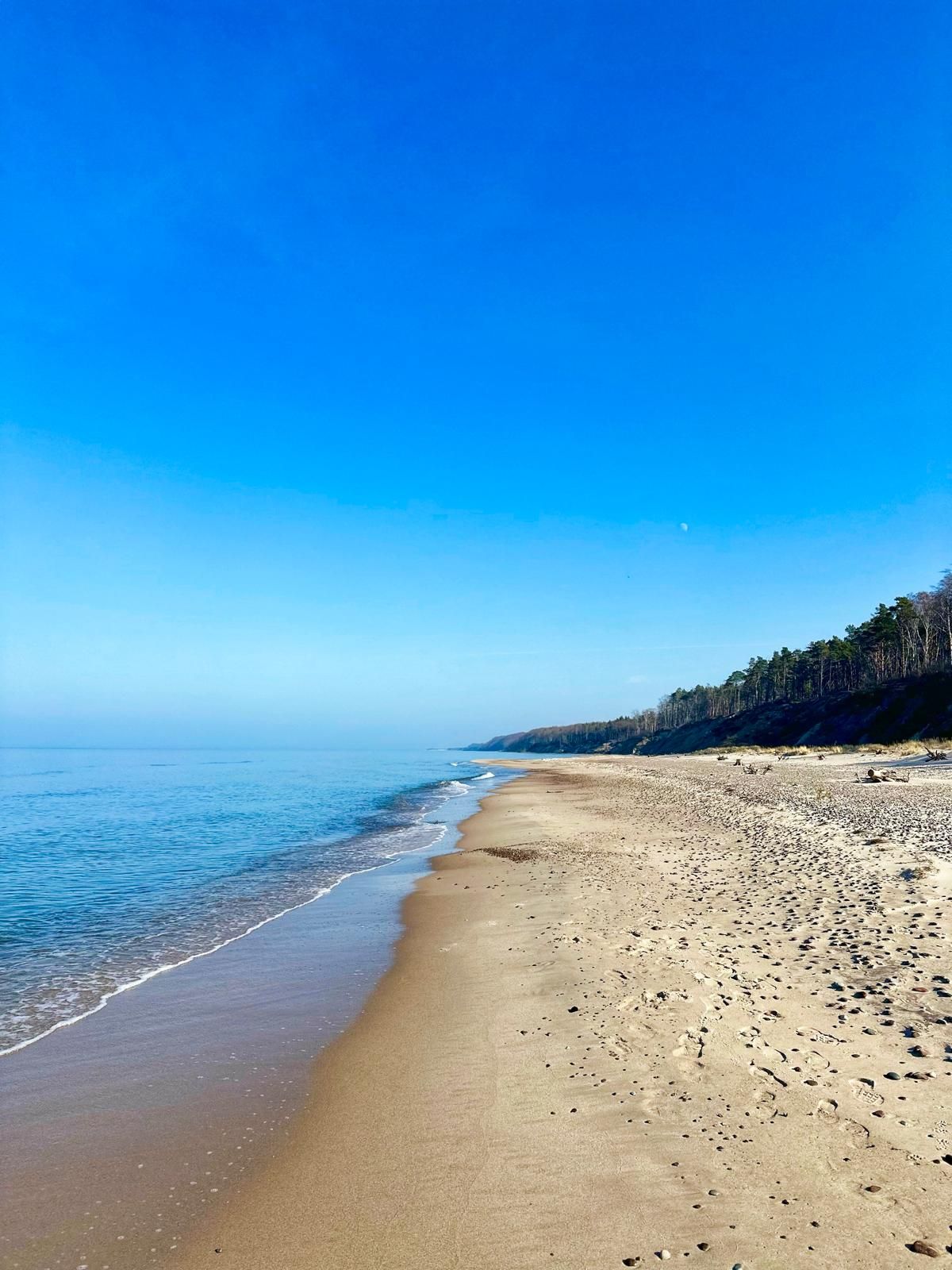 Szeroka, piaszczysta plaża i klif pod błękitnym niebem